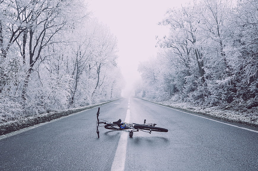 Fallen bicycle on empty winter road in snowy forest