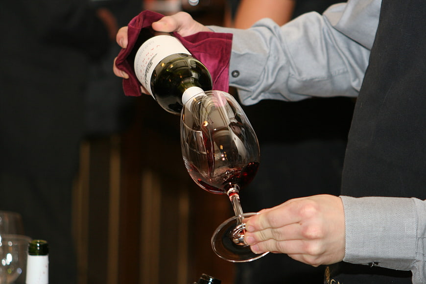 Sommelier pouring red wine into a glass with a cloth