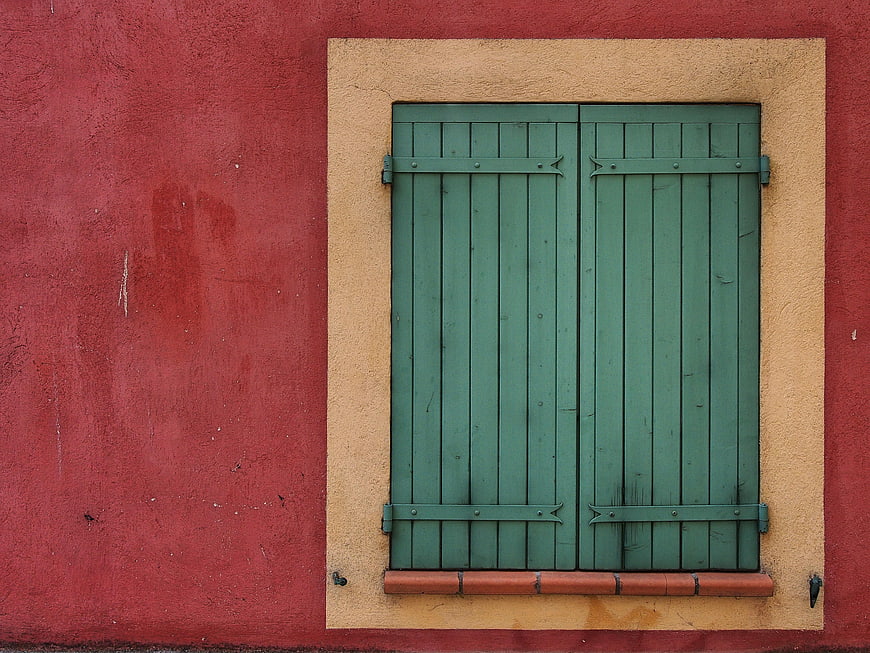 Green wooden shutters on a red textured wall