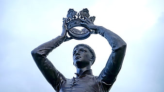Low angle view of bronze statue holding crown against sky