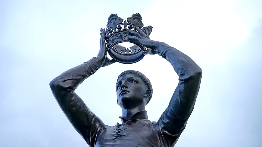 Low angle view of bronze statue holding crown against sky