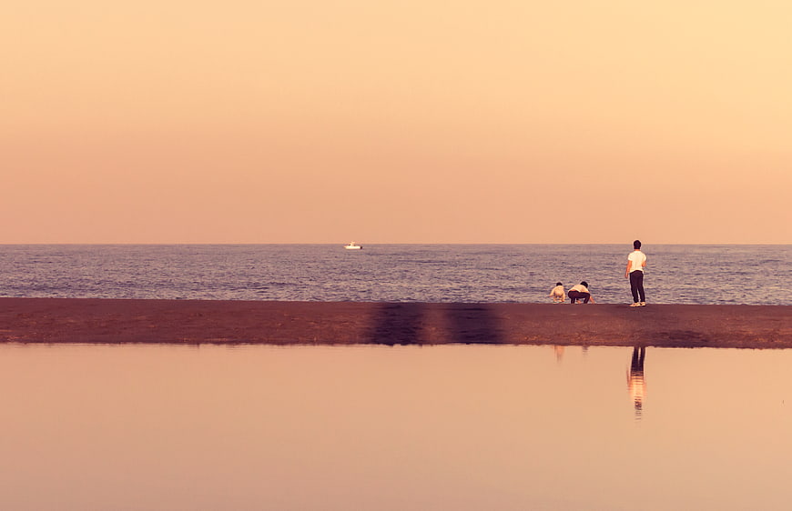 Silhouette of people on beach at sunset with water reflection