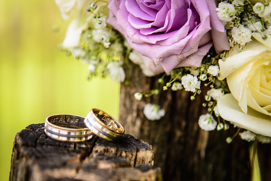 Wedding Rings on Wooden Stump with Purple and White Rose Bouquet