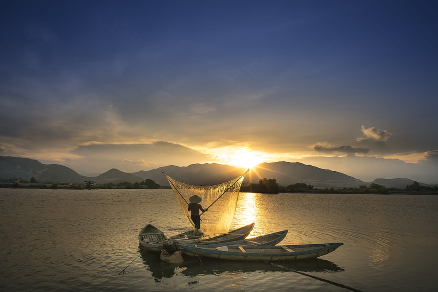 Fisherman Casting Net on Boat at Sunrise in Vietnam