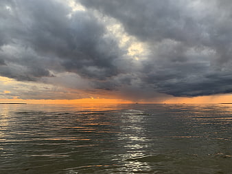 Dramatic sunset over ocean with storm clouds and rain