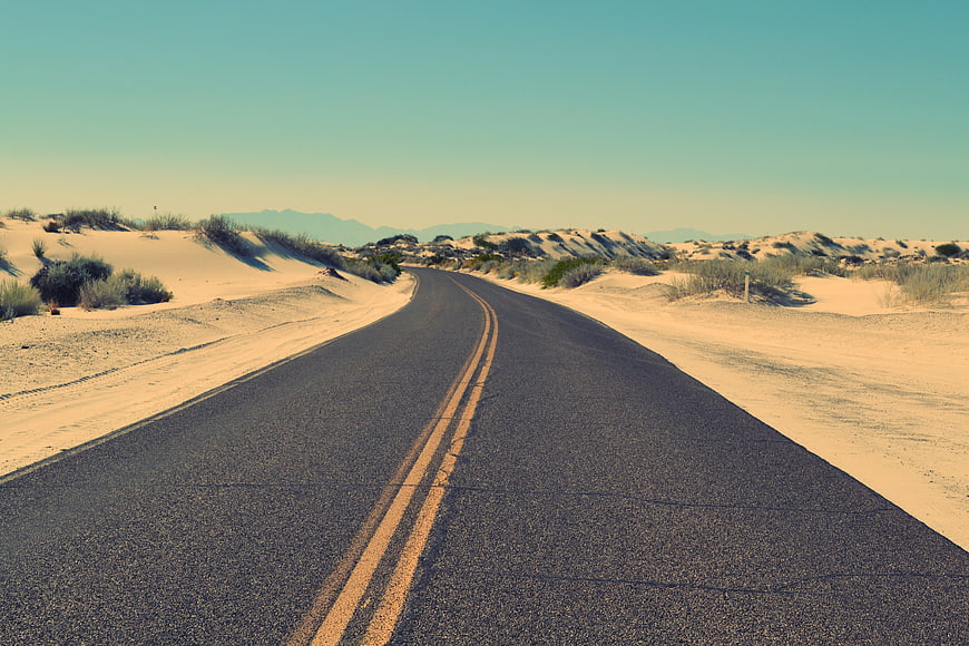 Empty asphalt road winding through desert sand dunes