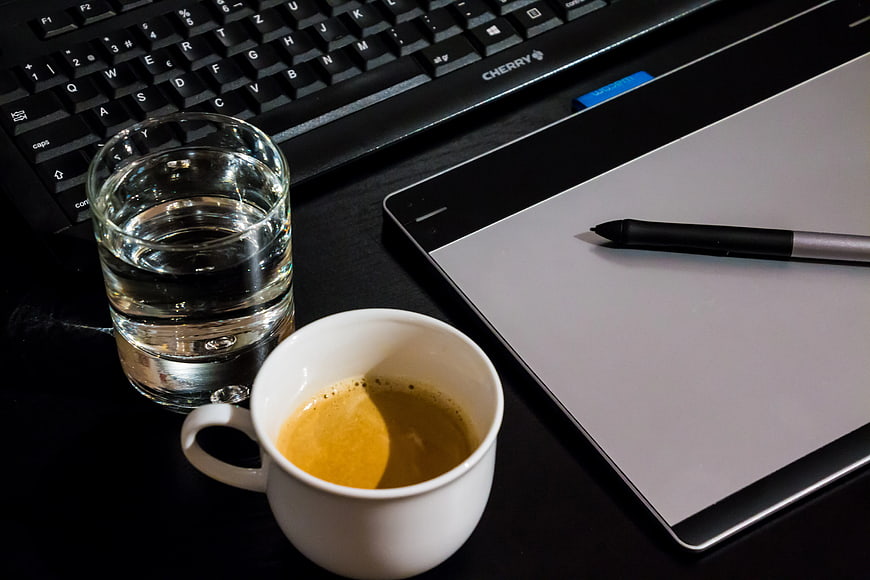Coffee cup, water glass, keyboard, and graphics tablet on desk