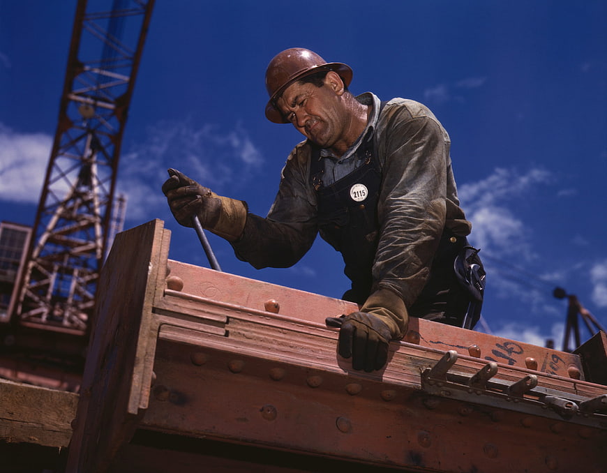 Construction worker riveting steel beam against blue sky