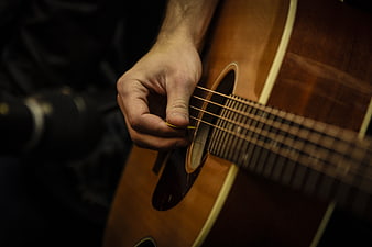 Close-up of hand playing acoustic guitar strings in dark studio