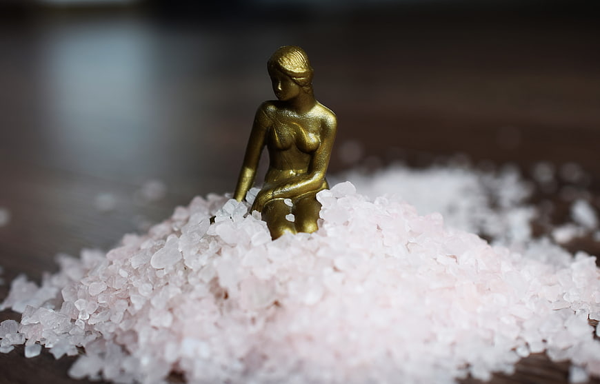 Golden female figurine sitting on pink Himalayan salt crystals