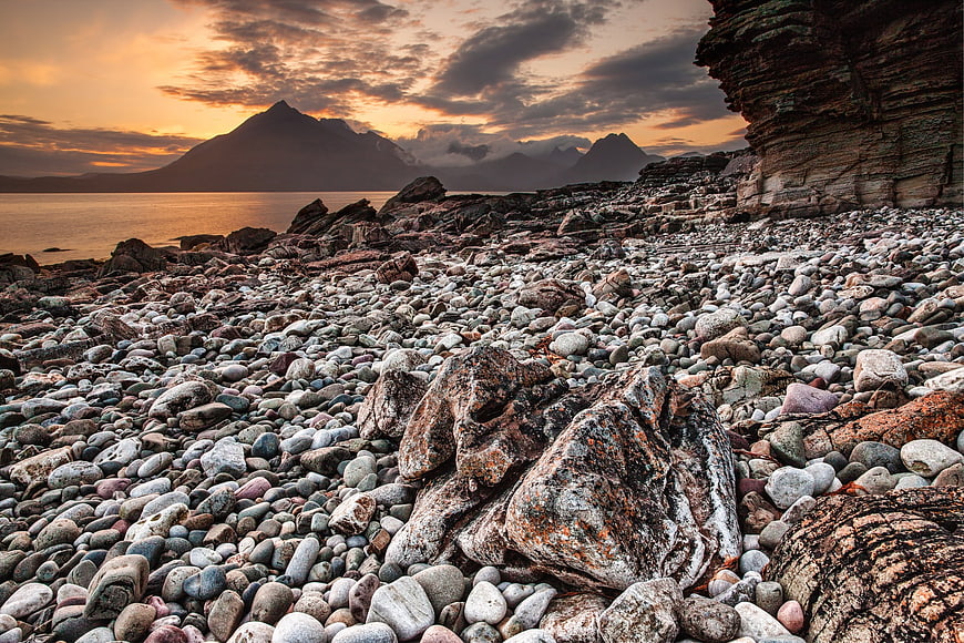 Dramatic sunset over rocky pebble beach with distant mountains