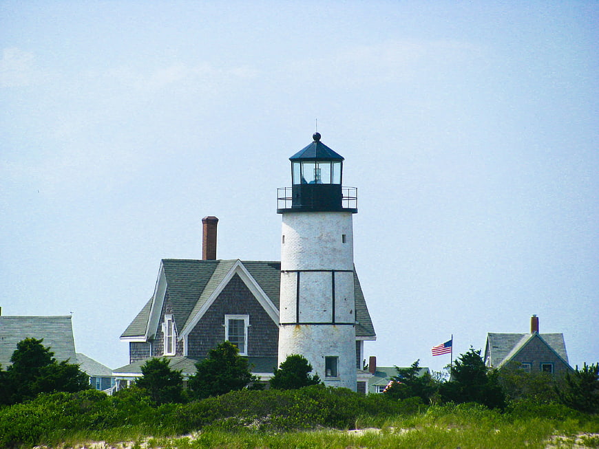White coastal lighthouse with keeper's house and American flag
