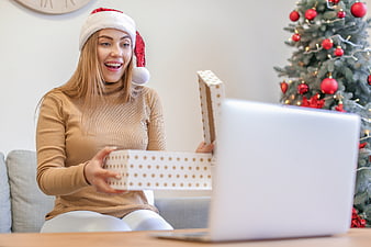 Happy woman in Santa hat opening gift box during video call