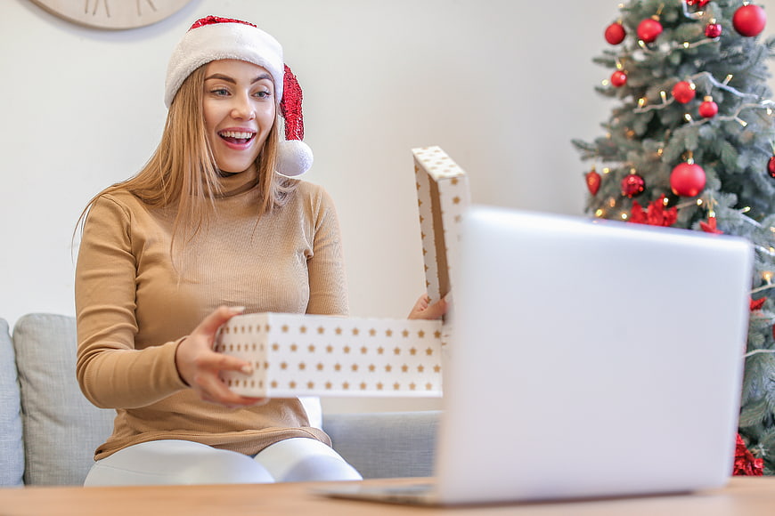 Happy woman in Santa hat opening gift box during video call