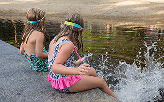 Two young girls splashing in a lake wearing swimsuits