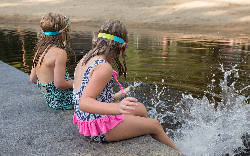 Two young girls splashing in a lake wearing swimsuits