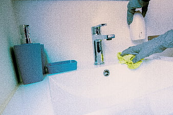 Gloved Hands Cleaning White Bathroom Sink with Yellow Cloth