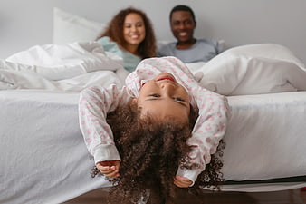 Happy young girl hanging upside down on bed with parents
