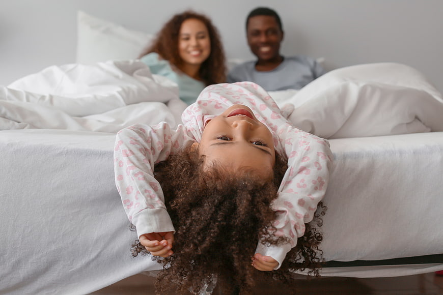 Happy young girl hanging upside down on bed with parents