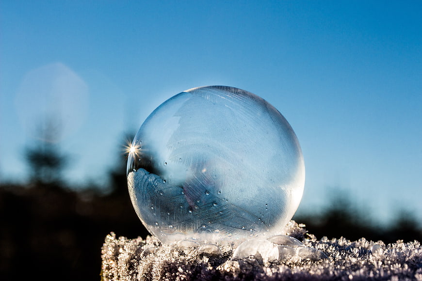 Frozen soap bubble on frosty surface with blue sky background