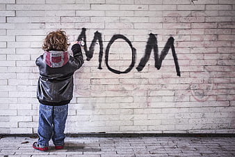 Child spray painting MOM graffiti on brick wall