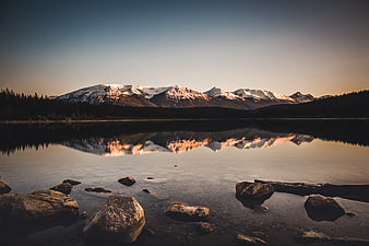 Snow-capped mountains reflecting in a calm lake at sunset