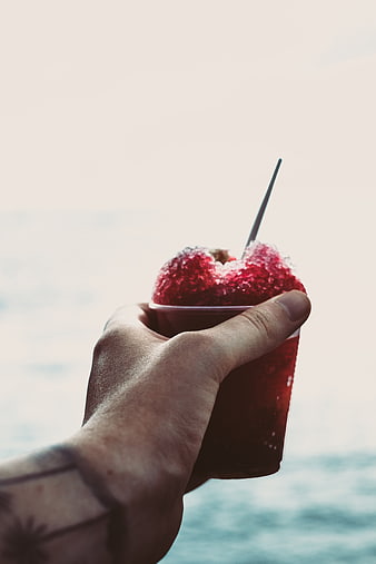 Hand holding red slushy drink by the ocean