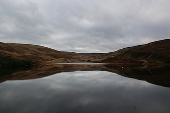Serene moorland lake with perfect reflection under cloudy sky