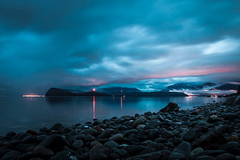 Serene Blue Hour Seascape with Rocky Shore and Distant Lights