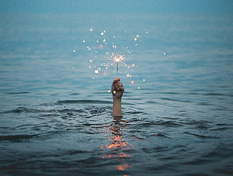 Hand holding sparkler in ocean water at dusk