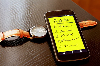 Smartphone with to-do list app and wristwatch on wooden table