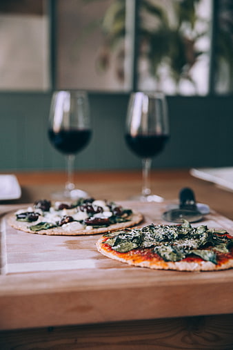 Two homemade pizzas and red wine on a wooden table