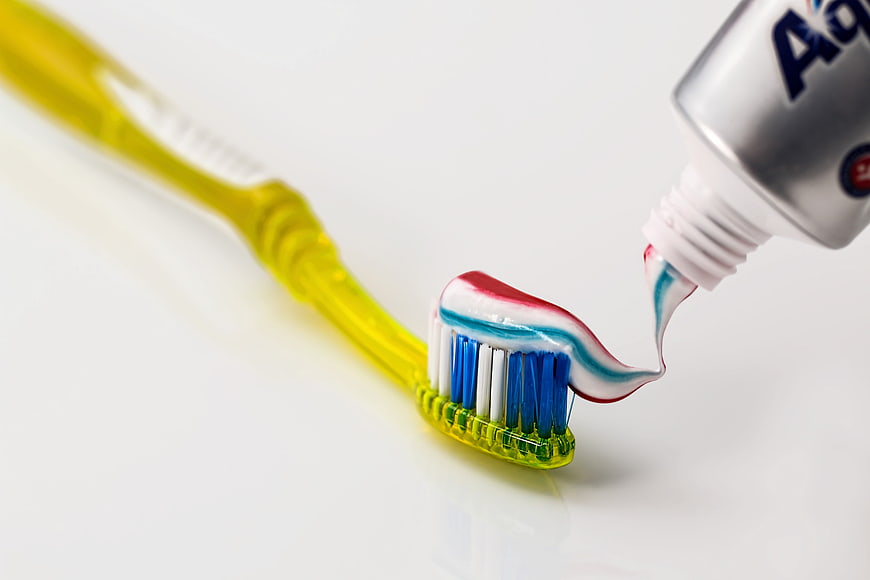 Toothpaste being squeezed onto a yellow toothbrush