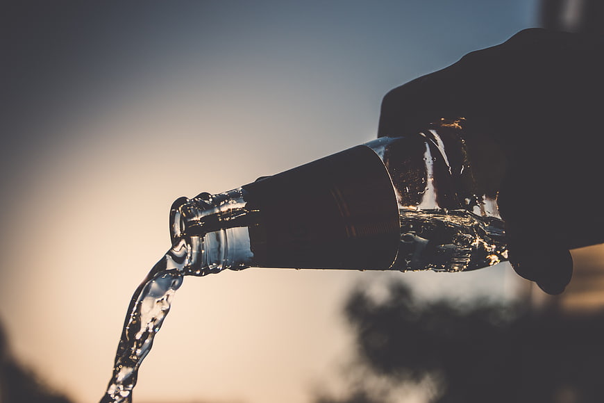 Hand Pouring Clear Liquid from Glass Bottle at Sunset