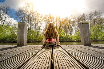 Girl sitting on wooden pier looking at river in spring