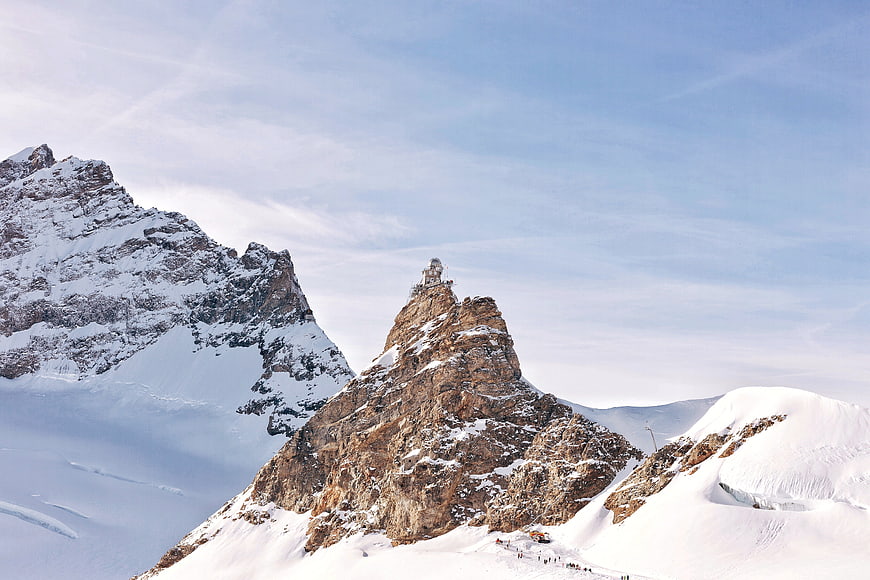 Snowy mountain peak with summit building and blue sky