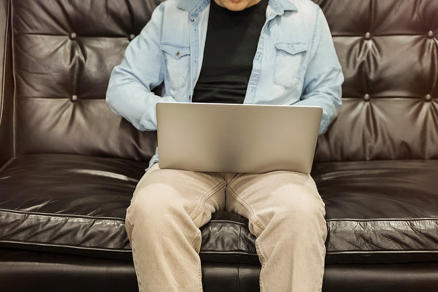 Man working on laptop sitting on leather sofa