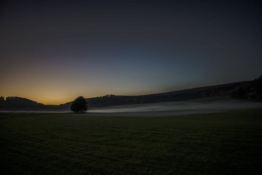 Misty landscape at dusk with fog rolling over green fields