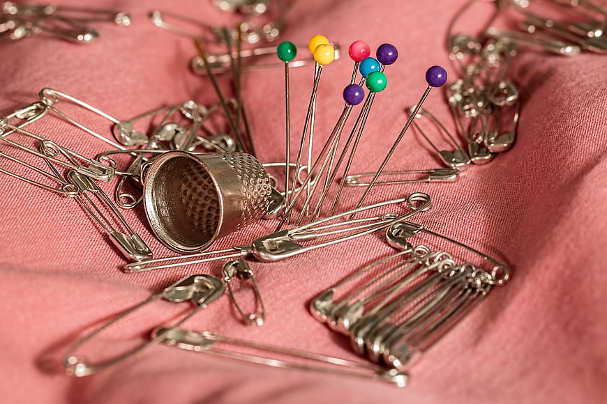 Sewing Thimble, Safety Pins, and Colorful Straight Pins on Pink Fabric
