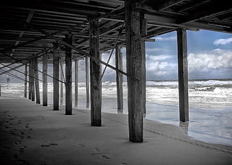 Underneath a weathered wooden pier on a sandy beach with ocean waves