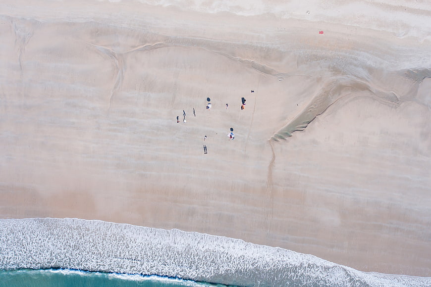 Aerial View of People Walking on Sandy Beach with Ocean Waves