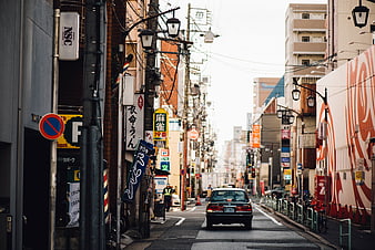 Green taxi driving down narrow Japanese street with signs