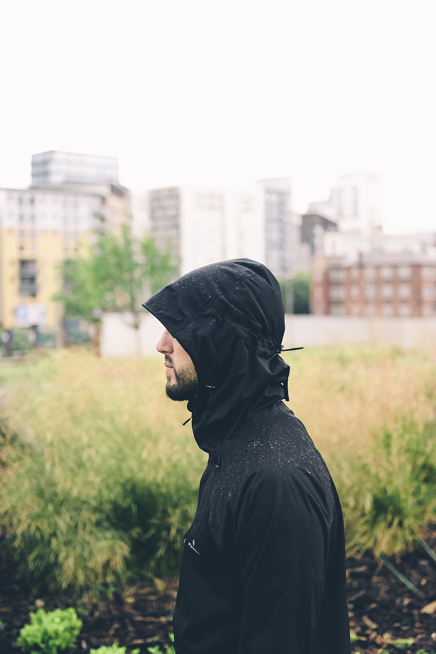 Man in Black Hooded Jacket Standing in Rainy Urban Garden