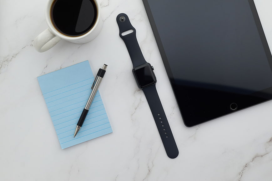 Flat lay of workspace with tablet, smartwatch, coffee, and notepad