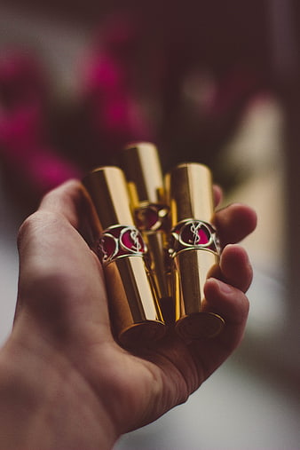 Hand holding luxury gold lipsticks with blurred background