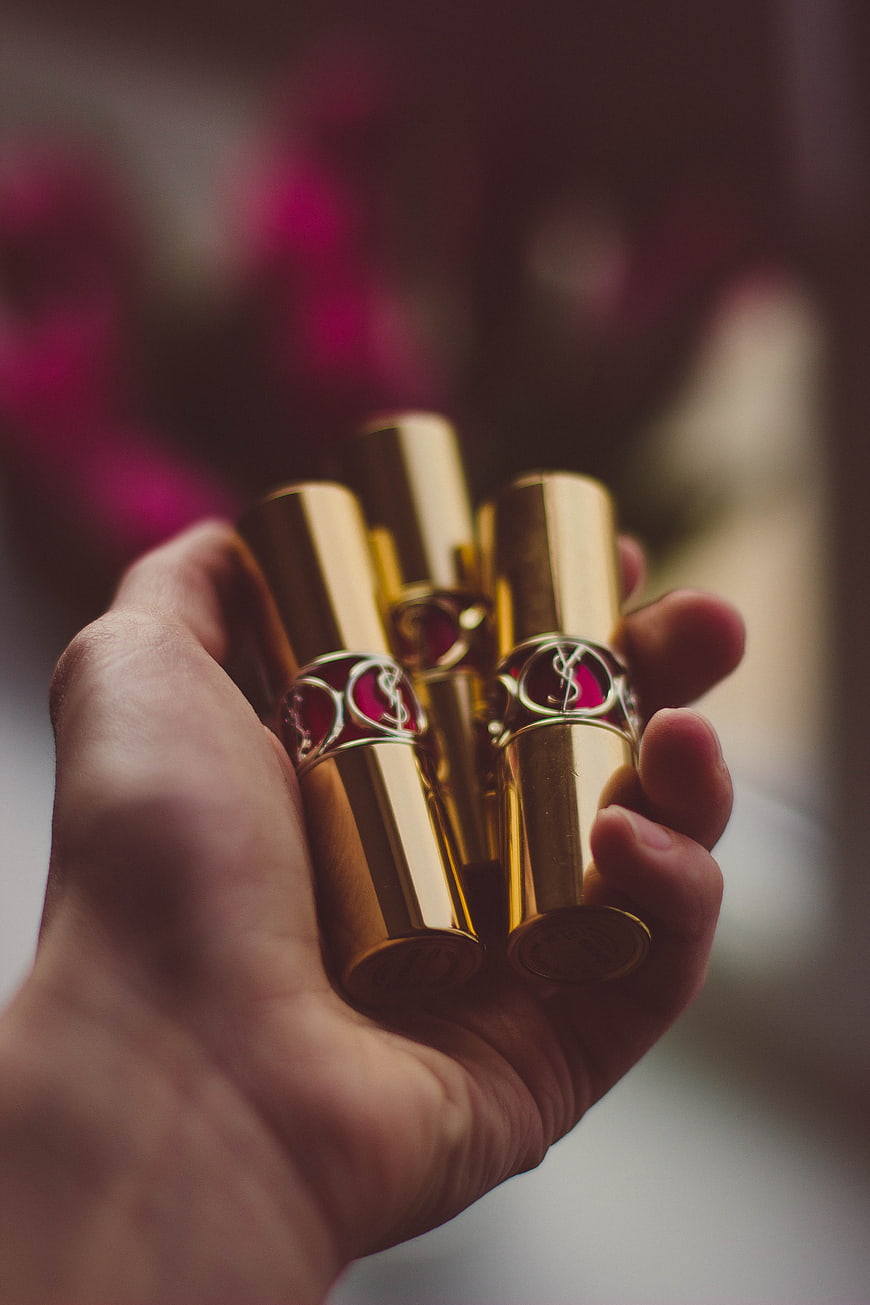Hand holding luxury gold lipsticks with blurred background
