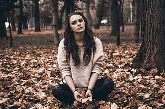 Young Woman Sitting in Autumn Forest with Fallen Leaves