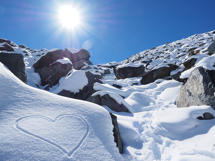 Heart drawn in snow on sunny mountain slope