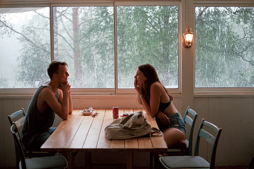 Couple sitting at wooden table in rainy cabin interior