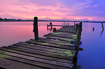 Wooden pier extending into calm lake at sunset with purple sky
